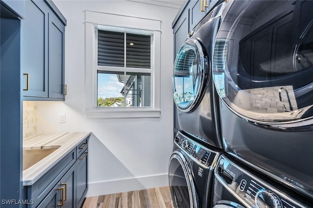 laundry room with a sink, cabinet space, wood finished floors, and stacked washer and clothes dryer