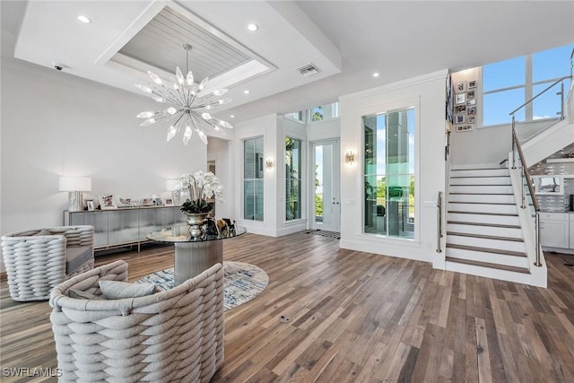 living area featuring a raised ceiling, visible vents, stairway, an inviting chandelier, and wood finished floors