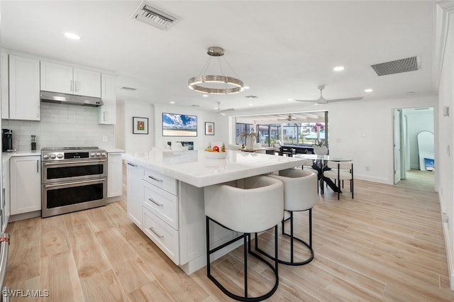 418 Germain Ave, Naples, FL 34108 - kitchen featuring double oven range, white cabinets, a kitchen breakfast bar, under cabinet range hood, and light countertops