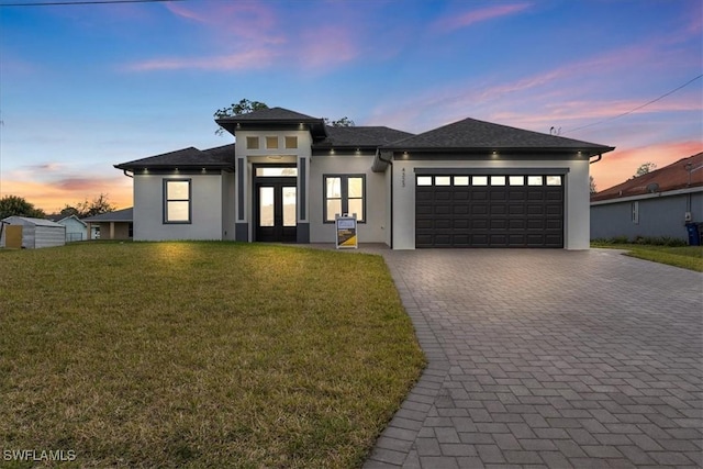 prairie-style home featuring a garage, decorative driveway, a front yard, and stucco siding