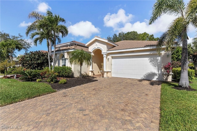 mediterranean / spanish-style home with a garage, a tiled roof, decorative driveway, stucco siding, and a front lawn