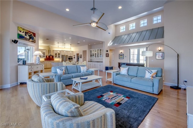 living room with light wood-type flooring, a towering ceiling, and ceiling fan