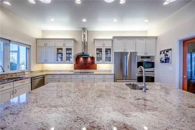 kitchen with sink, wall chimney exhaust hood, stainless steel appliances, and light stone countertops