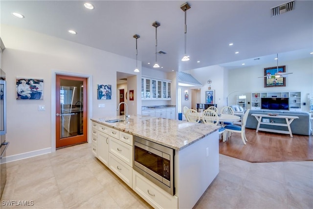 kitchen with hanging light fixtures, light stone countertops, stainless steel microwave, sink, and a kitchen island with sink