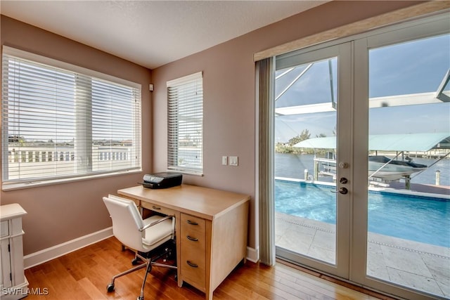 home office featuring a water view, light hardwood / wood-style floors, and french doors