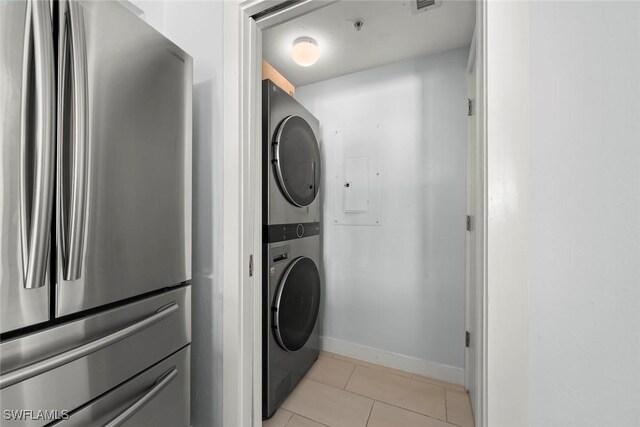 laundry room with light tile patterned floors, laundry area, baseboards, visible vents, and stacked washing maching and dryer