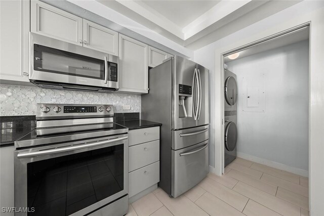 kitchen with dark countertops, appliances with stainless steel finishes, stacked washing maching and dryer, and backsplash