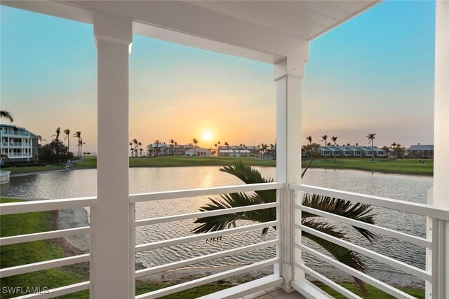 balcony at dusk featuring a water view