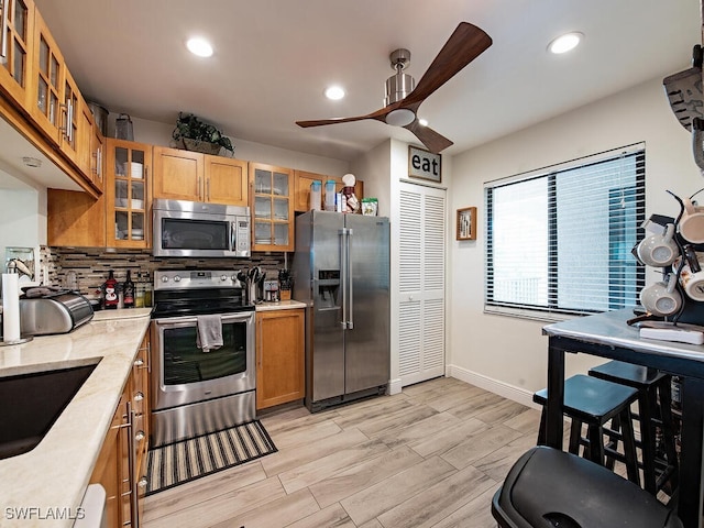 kitchen with light countertops, appliances with stainless steel finishes, glass insert cabinets, and decorative backsplash