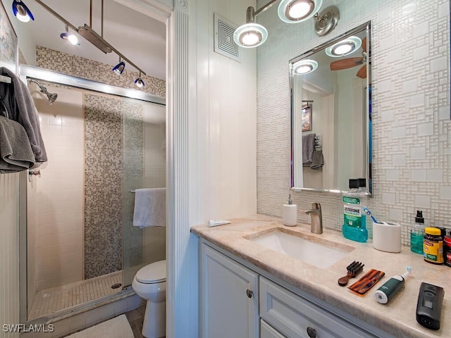 bathroom featuring toilet, vanity, visible vents, backsplash, and a stall shower