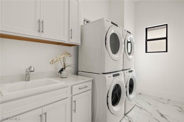 washroom with cabinet space, baseboards, marble finish floor, stacked washing maching and dryer, and a sink