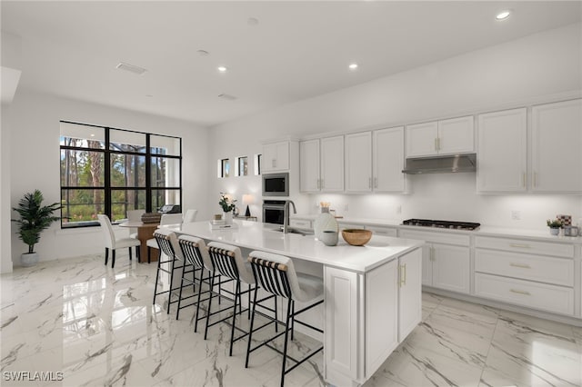 kitchen featuring light countertops, white cabinetry, gas cooktop, an island with sink, and under cabinet range hood