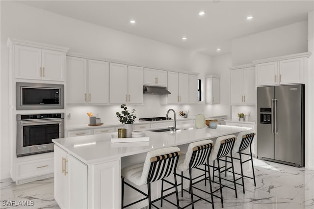 kitchen with light countertops, appliances with stainless steel finishes, white cabinetry, an island with sink, and under cabinet range hood