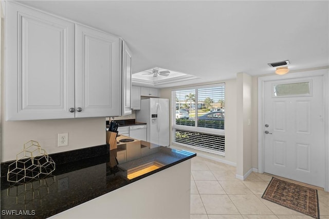 kitchen with light tile patterned floors, ceiling fan, white cabinetry, white fridge with ice dispenser, and a raised ceiling