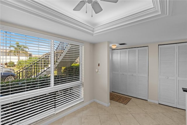 doorway to outside with ceiling fan, ornamental molding, a raised ceiling, and light tile patterned floors