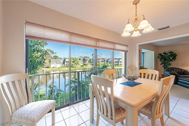 dining area featuring a textured ceiling, a water view, a chandelier, and light tile patterned floors