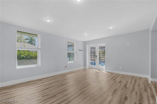 spare room featuring plenty of natural light, light wood-style flooring, baseboards, and french doors