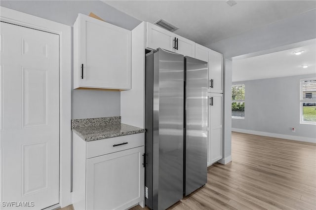 kitchen with stone counters, freestanding refrigerator, white cabinetry, light wood-type flooring, and baseboards