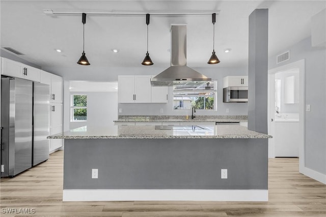 kitchen featuring appliances with stainless steel finishes, a healthy amount of sunlight, white cabinetry, a sink, and island range hood