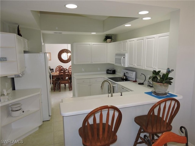 kitchen with a breakfast bar area, white cabinets, white appliances, and kitchen peninsula