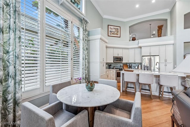 dining area with a towering ceiling, ornamental molding, and light hardwood / wood-style floors