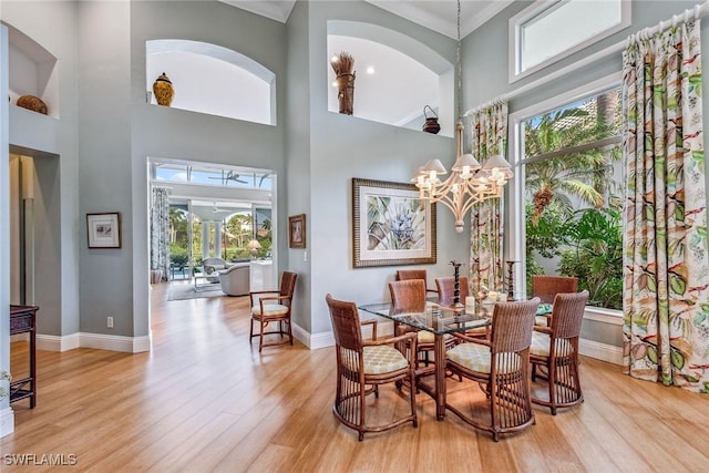 dining room with ornamental molding, a chandelier, light hardwood / wood-style flooring, and a high ceiling