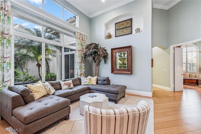 living room with crown molding, light wood-type flooring, and a towering ceiling