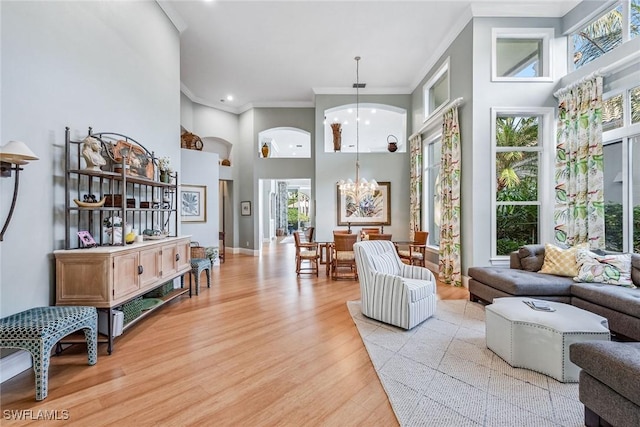 living room featuring a towering ceiling, ornamental molding, light wood-type flooring, and a notable chandelier