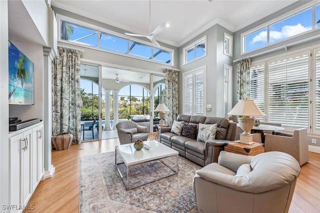 living room featuring crown molding, light hardwood / wood-style flooring, a towering ceiling, ceiling fan, and decorative columns