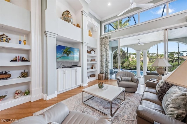 living room featuring built in shelves, ceiling fan, a healthy amount of sunlight, and a high ceiling