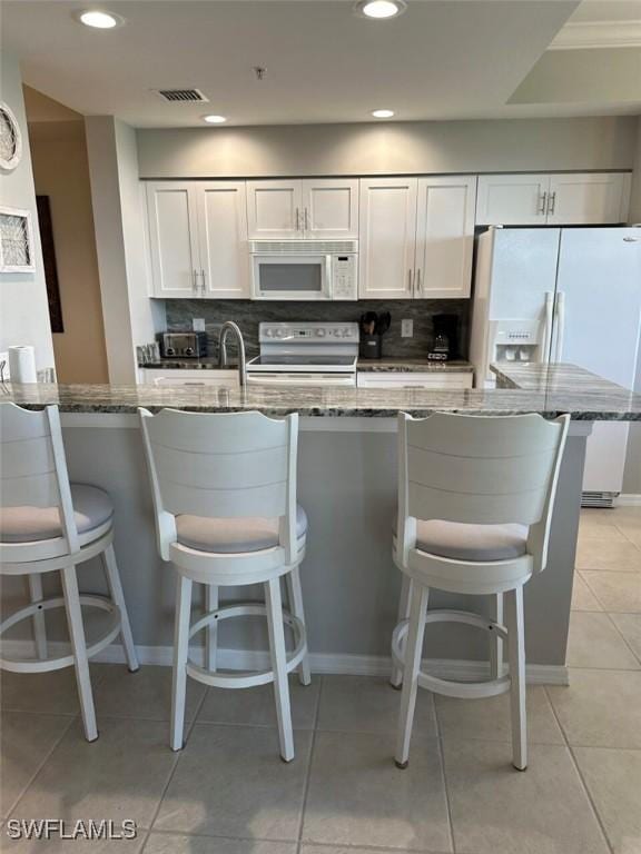 kitchen with white appliances, visible vents, dark stone counters, white cabinets, and tasteful backsplash