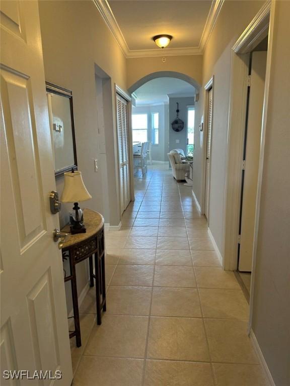 corridor featuring baseboards, arched walkways, crown molding, and light tile patterned flooring