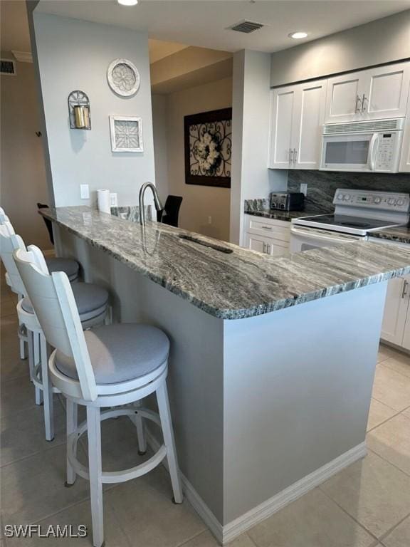 kitchen featuring a sink, white cabinetry, dark stone counters, white appliances, and a breakfast bar area