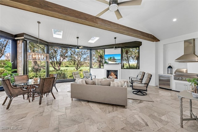 living area featuring lofted ceiling with skylight, recessed lighting, a warm lit fireplace, and ceiling fan