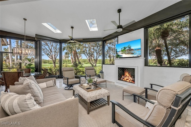 sunroom / solarium with a wealth of natural light, a warm lit fireplace, a skylight, and ceiling fan with notable chandelier