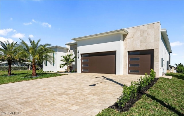 contemporary home with stucco siding, a front yard, decorative driveway, and a garage