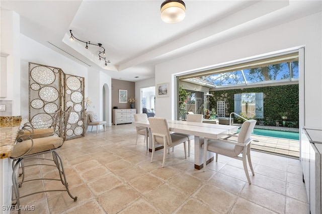 dining area with rail lighting, a tray ceiling, and arched walkways