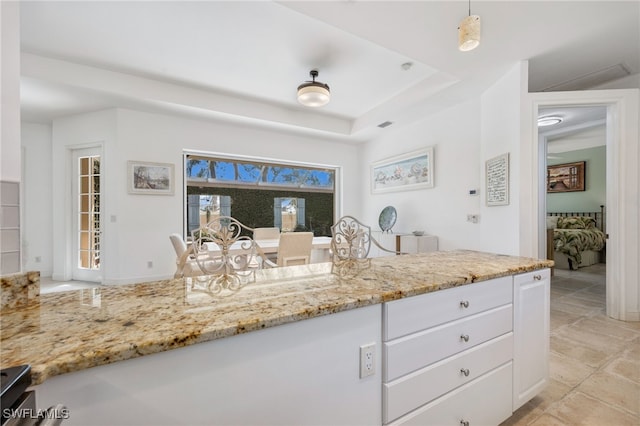 kitchen featuring a raised ceiling, white cabinetry, and light stone countertops