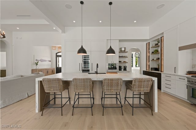 kitchen featuring a large island, arched walkways, open shelves, and decorative light fixtures