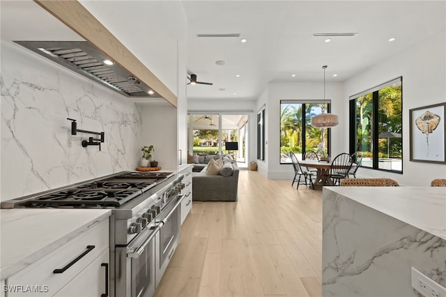 kitchen with light stone counters, range with two ovens, hanging light fixtures, decorative backsplash, and white cabinetry