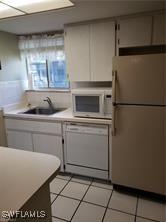 kitchen with light tile patterned flooring, sink, white cabinets, and white appliances