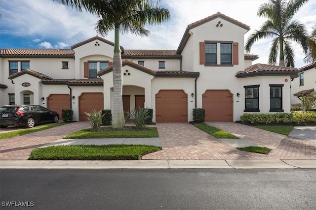 mediterranean / spanish house featuring decorative driveway, a tiled roof, an attached garage, and stucco siding