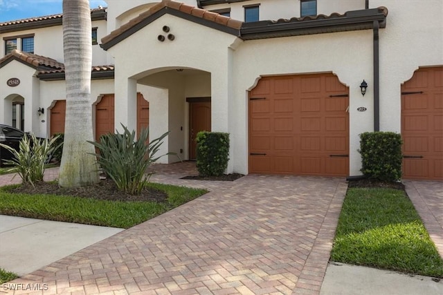 view of front of home featuring a garage, a tiled roof, decorative driveway, and stucco siding