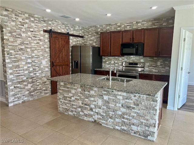 kitchen with sink, a center island with sink, stainless steel appliances, a barn door, and light stone countertops