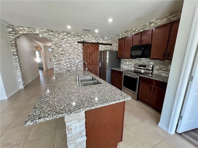 kitchen featuring sink, light stone counters, appliances with stainless steel finishes, an island with sink, and a barn door