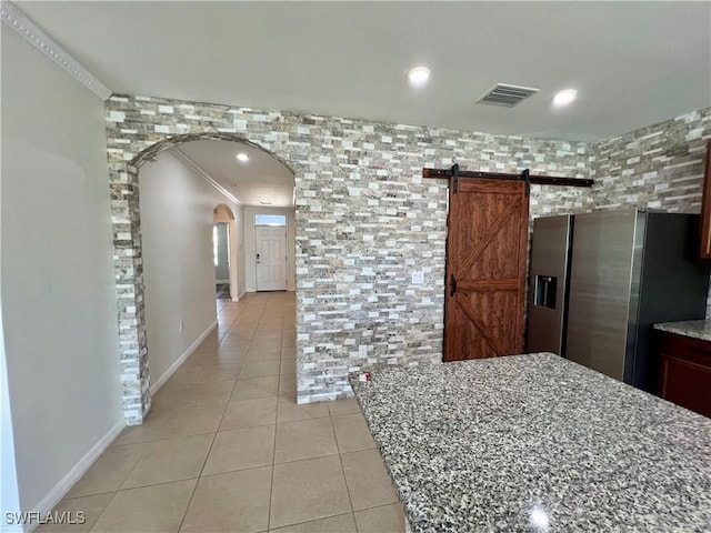 kitchen featuring light tile patterned floors, stainless steel fridge, light stone countertops, and a barn door