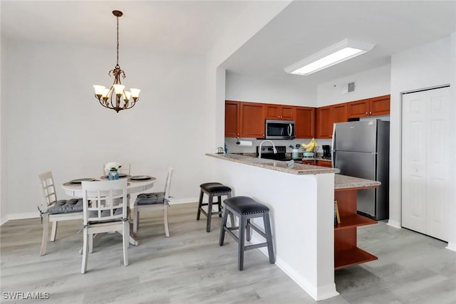 kitchen featuring appliances with stainless steel finishes, a breakfast bar, light hardwood / wood-style flooring, kitchen peninsula, and hanging light fixtures