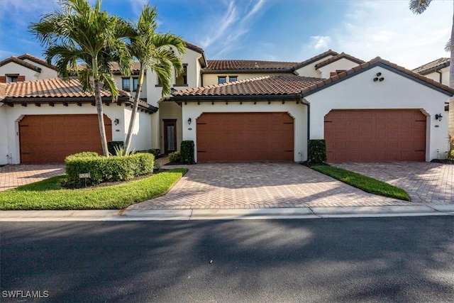 mediterranean / spanish-style home featuring a garage, decorative driveway, a tiled roof, and stucco siding