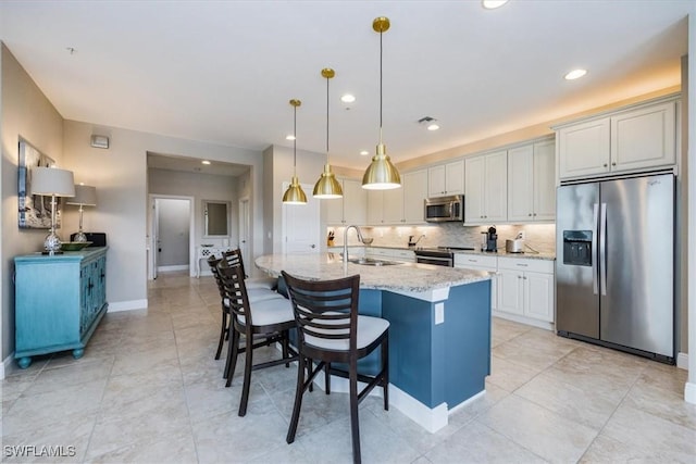 kitchen with light stone counters, pendant lighting, a center island with sink, appliances with stainless steel finishes, and white cabinetry