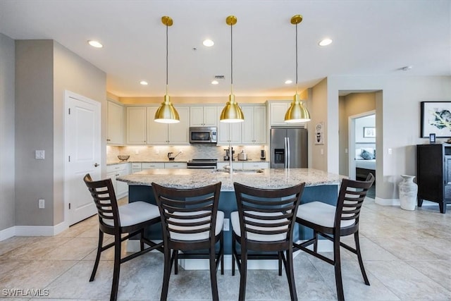 kitchen featuring decorative light fixtures, stainless steel appliances, white cabinets, a kitchen island with sink, and light stone countertops